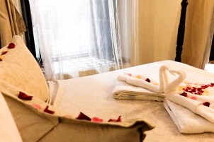 Una camera d'albergo con un letto, un cuscino e un asciugamano decorato con petali di rosa.