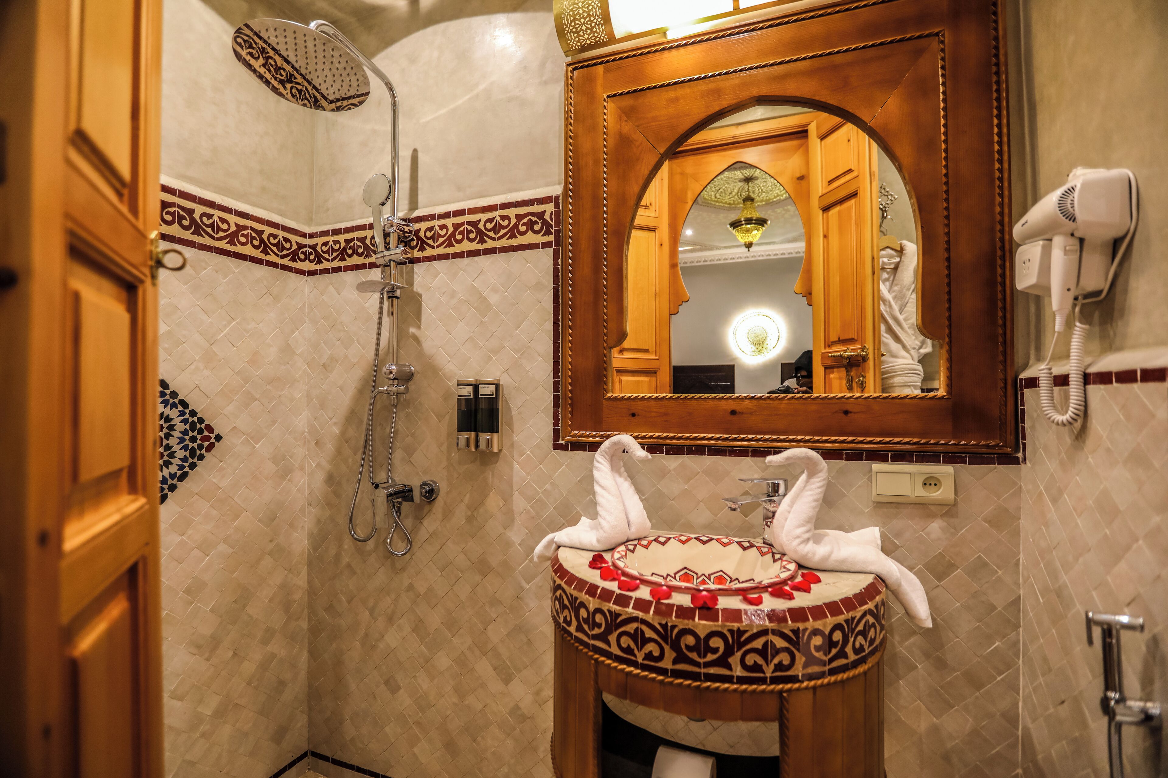 Un baño con ducha, lavabo con azulejos decorativos, espejo y secador de pelo.