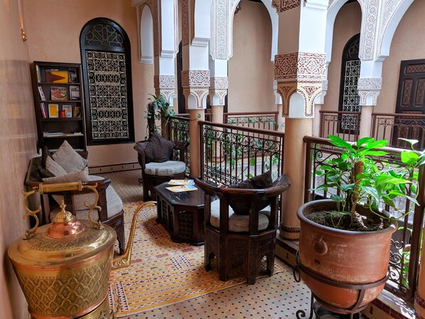 A traditional Moroccan interior with a patterned floor, wooden furniture, a brass container, and a potted plant.