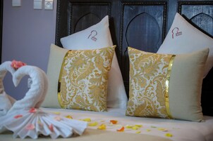 Una cama con almohadas decorativas, una toalla con forma de cisne y pétalos de flores esparcidos.