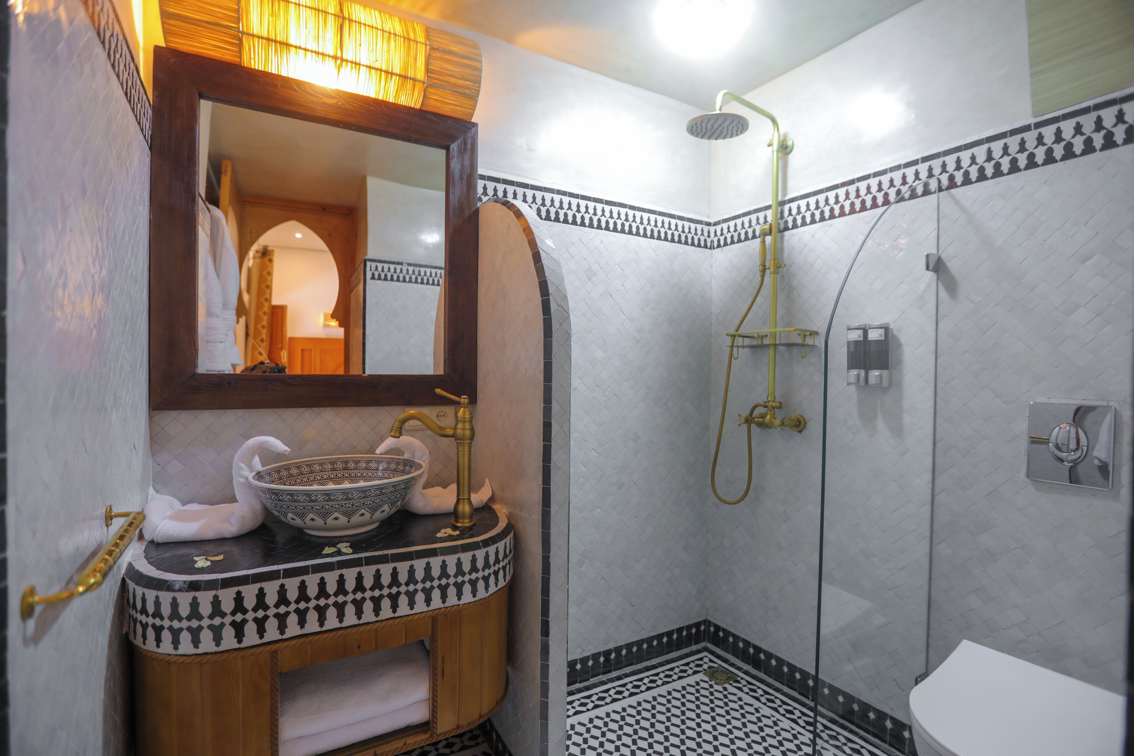 A bathroom with a wooden vanity, a bowl sink, a mirror, a shower with a glass door, and patterned tiles.