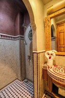 Un baño con ducha, un lavabo con un espejo decorativo y baldosas estampadas en paredes y suelo.