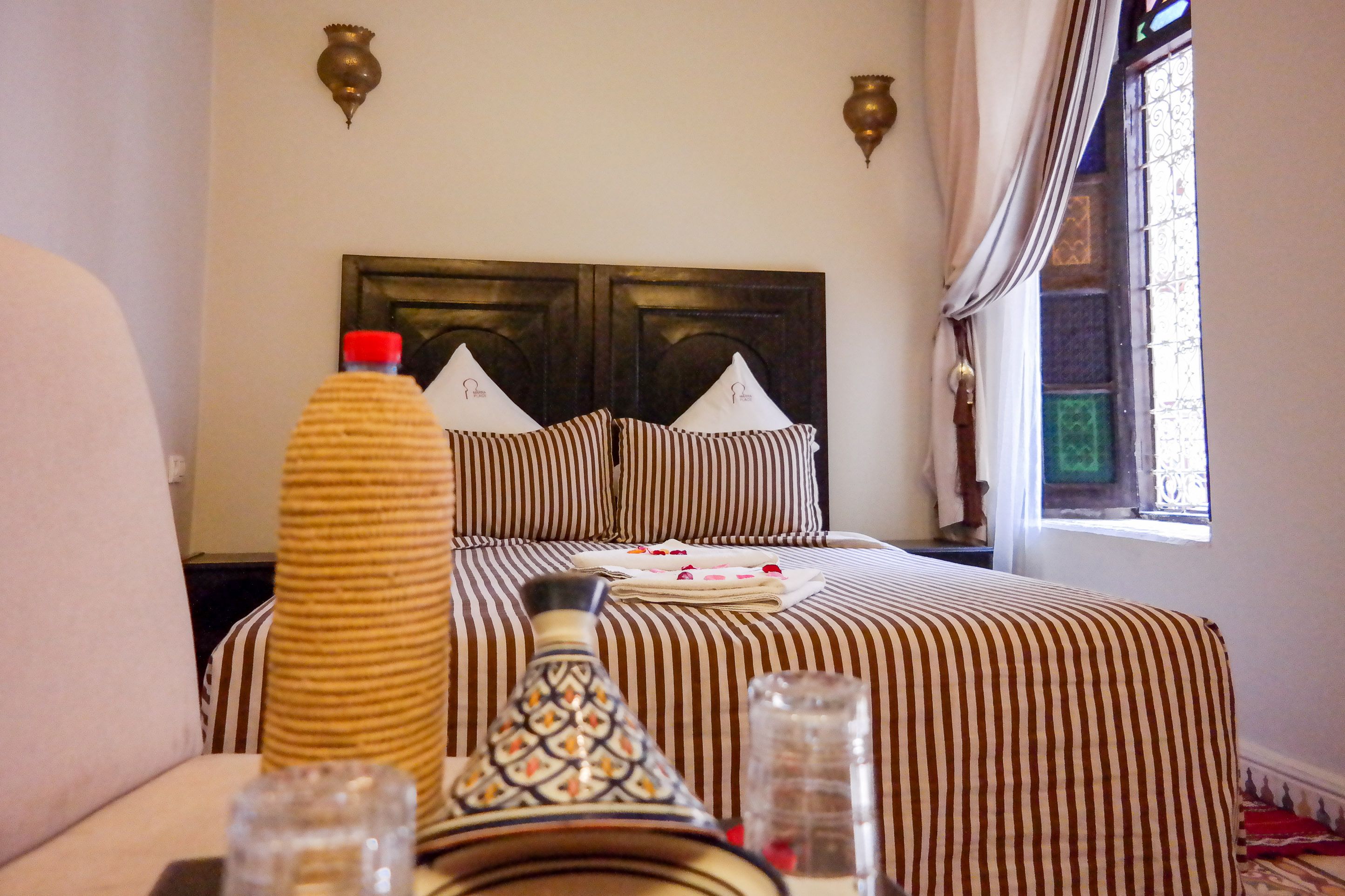A hotel room with a bed featuring striped bedding, a decorative headboard, and a window with a view.