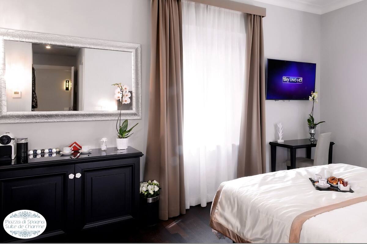 Una habitación de hotel con cama, televisión, cómoda y ventana con cortinas.