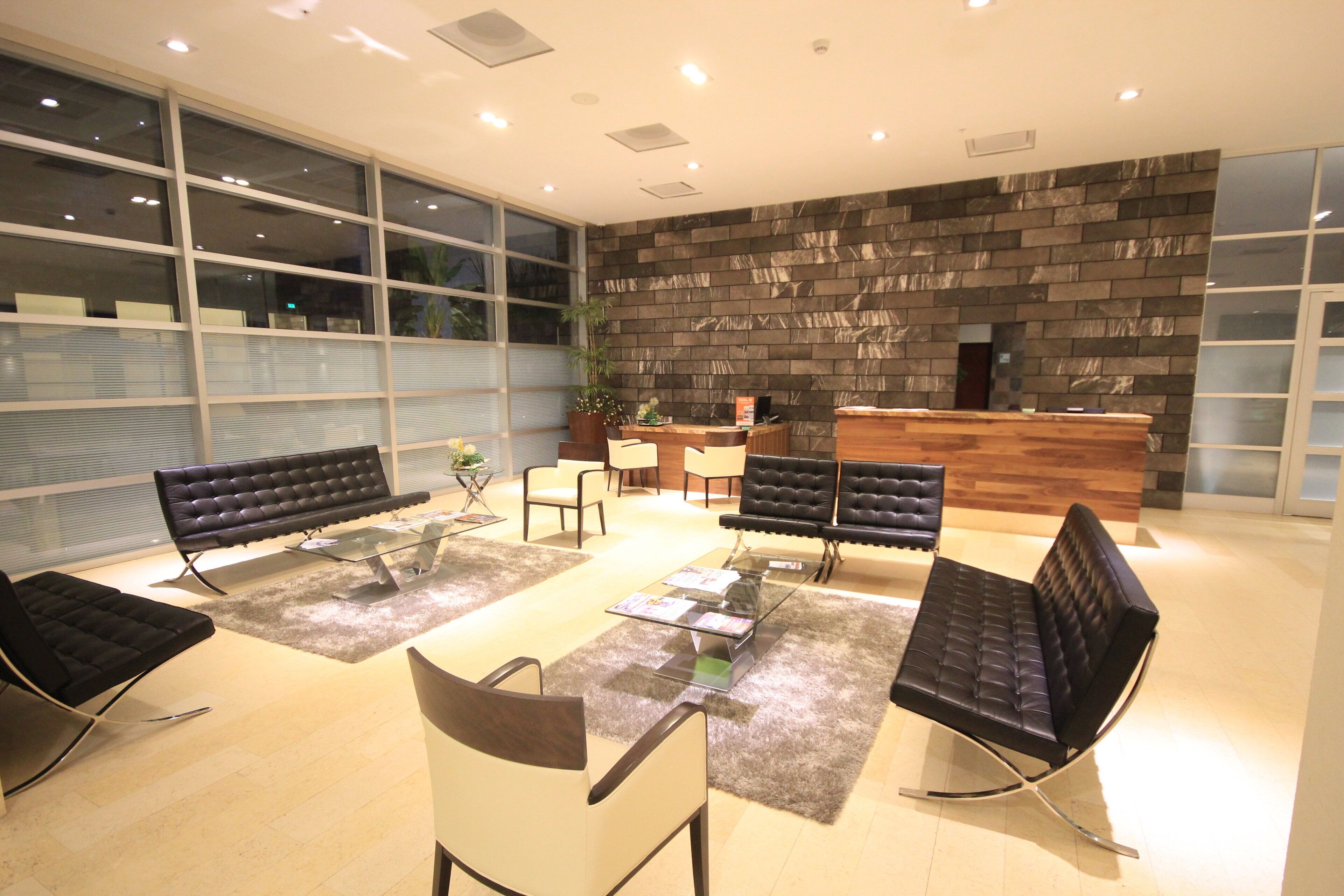 Un espace d’accueil moderne avec un mur en pierre, des canapés en cuir noir et une table basse en verre.