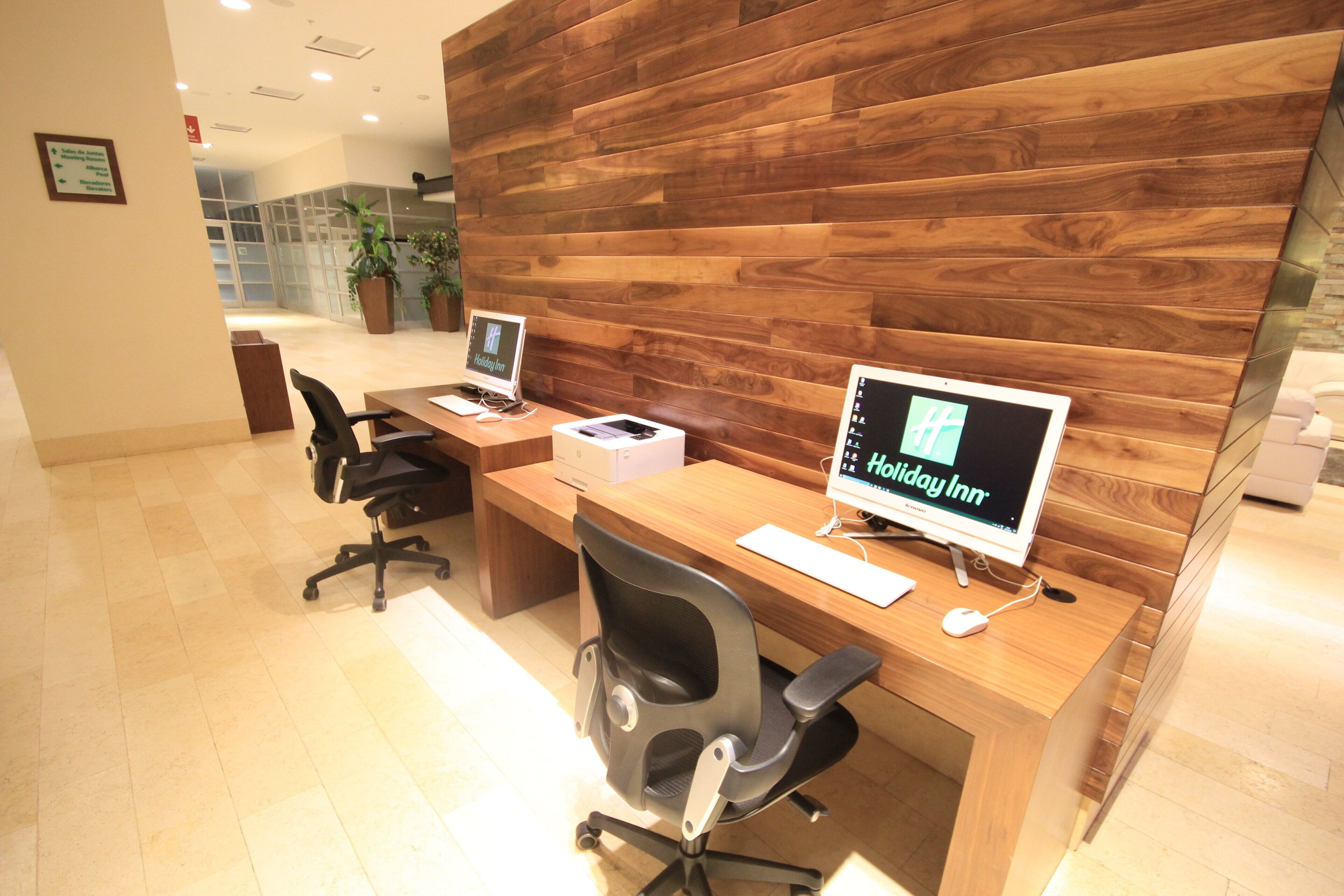 A reception desk with two computer monitors displaying the Holiday Inn logo, a wooden panel wall, and a tiled floor.