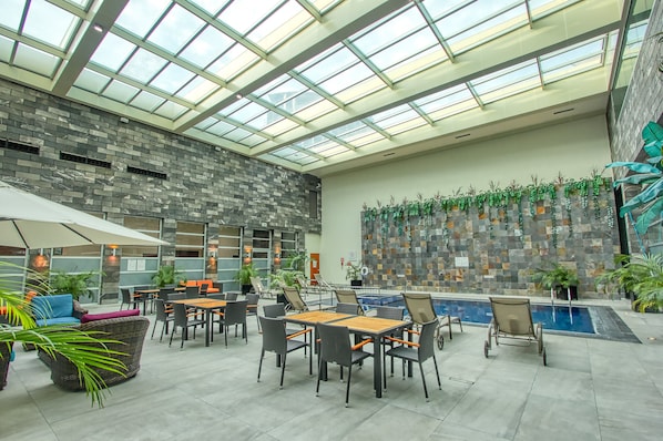An indoor patio area with a glass ceiling, stone wall, and a pool. - Holiday Inn Leon Plaza Mayor by IHG (León)