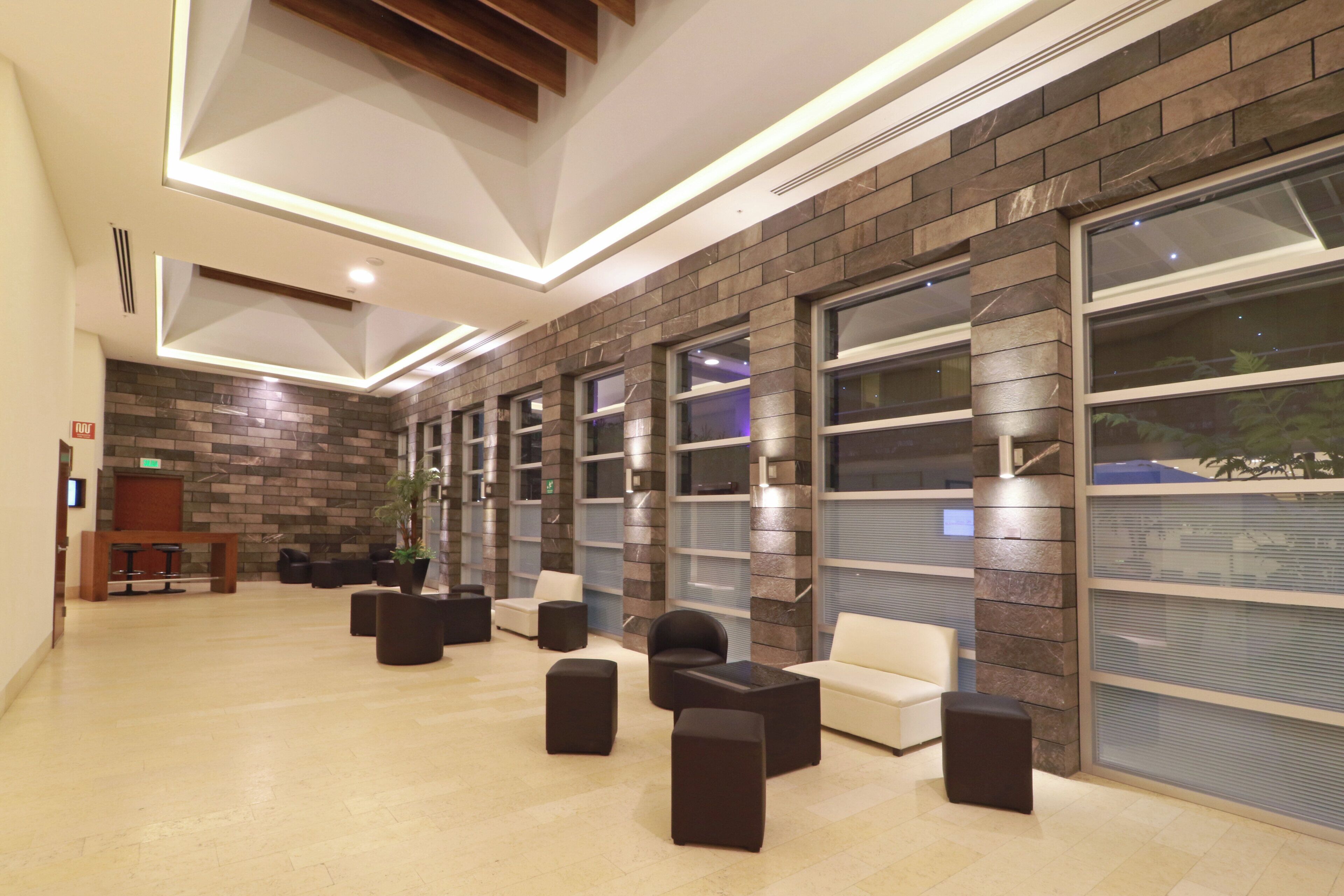 A modern lobby with a brick wall, large windows, and a seating area with sofas and ottomans.