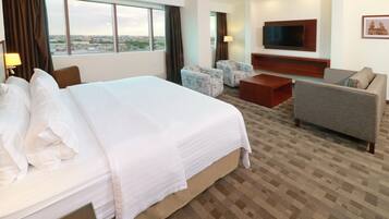 Habitación de hotel con una cama grande, dos sillones, un sofá, televisión y vista a la ciudad.