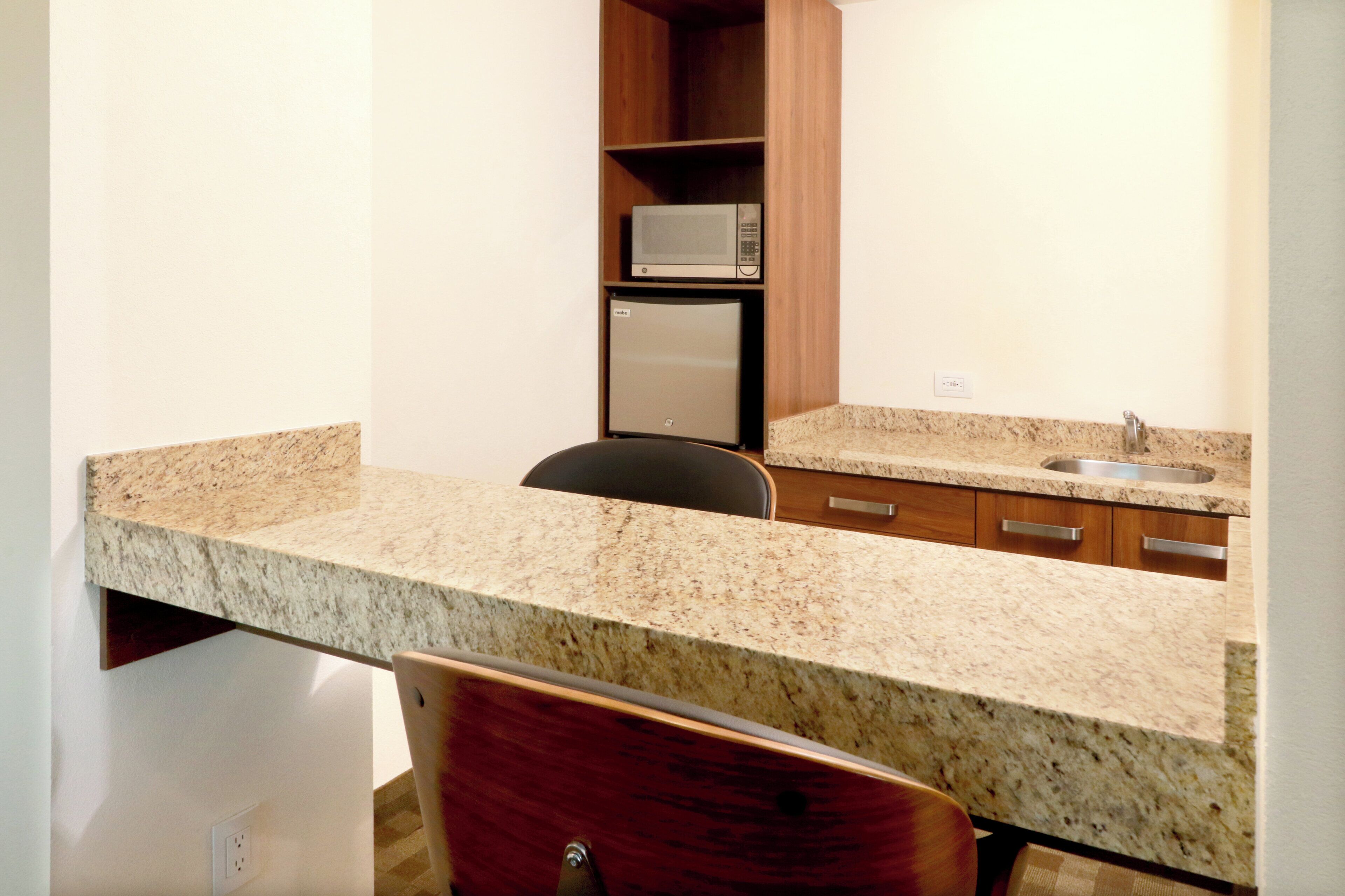 Cocina compacta con encimera de granito, microondas y lavabo.