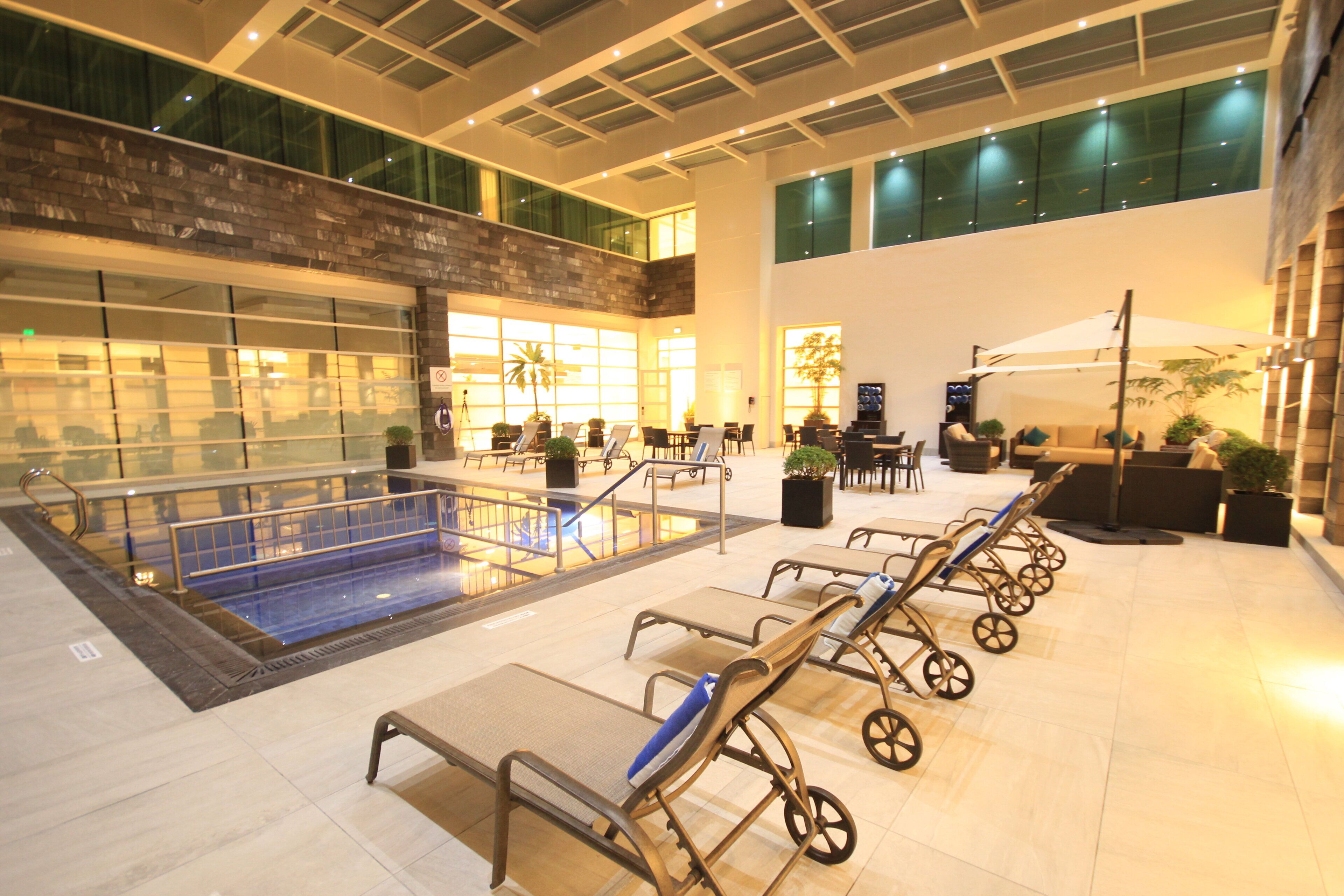 A spacious indoor area with a pool, sun loungers, and a seating area with tables and chairs.