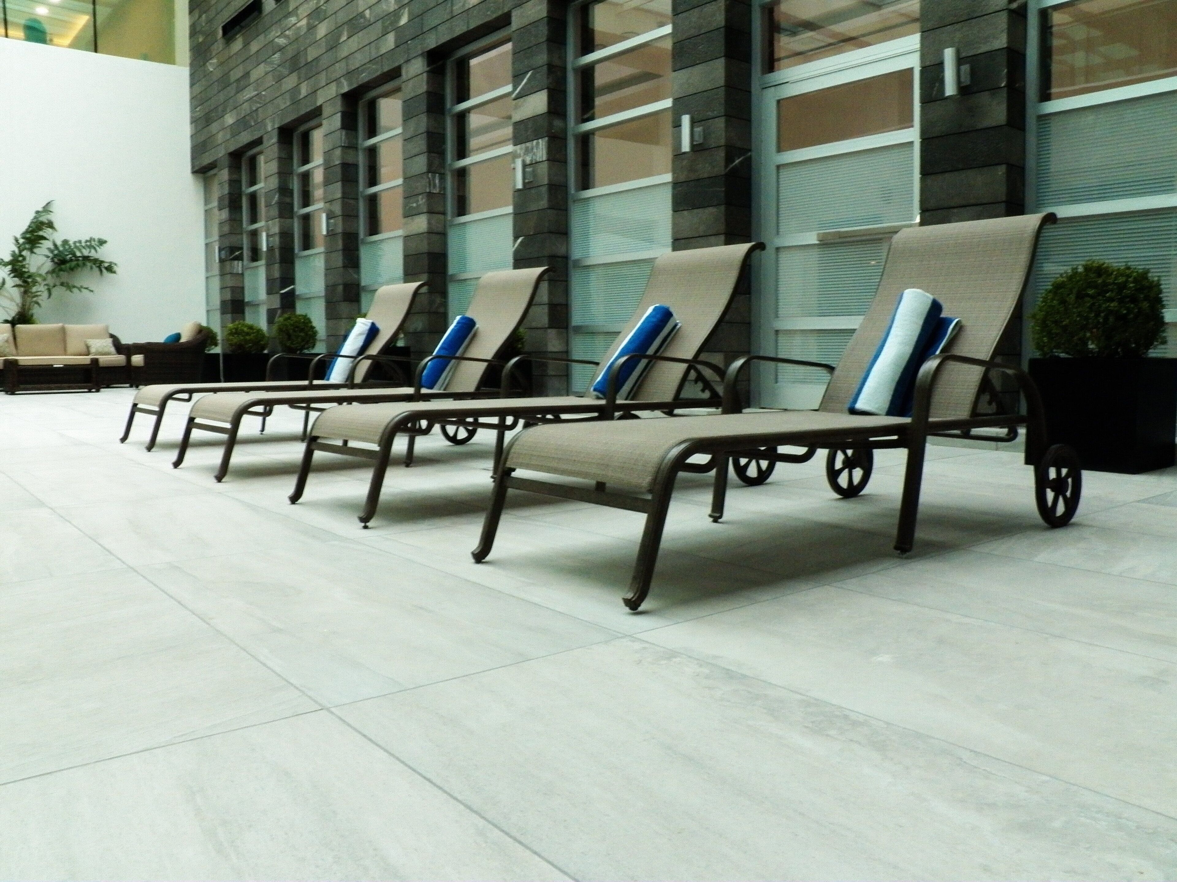 A row of sun loungers with wheels, a potted plant, and a building with large windows in the background.