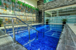 An indoor swimming pool with blue tiles, metal railings, and a stone wall with greenery. - Holiday Inn Leon Plaza Mayor by IHG (León)