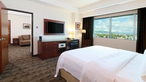 Een hotelkamer met een groot bed, een bureau met een computer, een televisie en uitzicht op de stad.