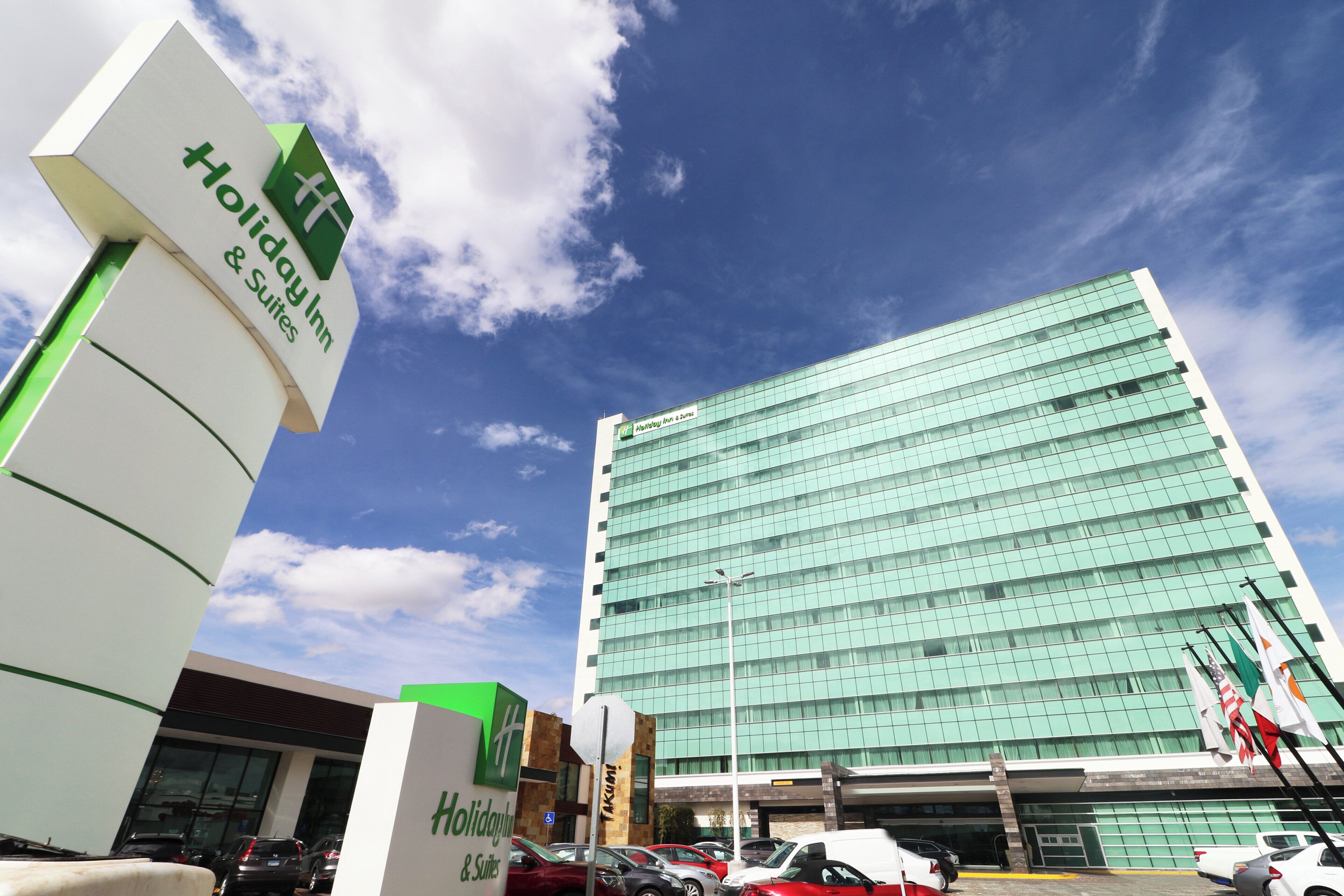 Un hotel Holiday Inn & Suites con fachada de vidrio moderna, un estacionamiento subterráneo y varias banderas.