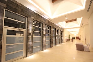 A hallway with a modern design, featuring a combination of brick and glass elements, and a seating area with a table and chairs. - Holiday Inn Leon Plaza Mayor by IHG (León)