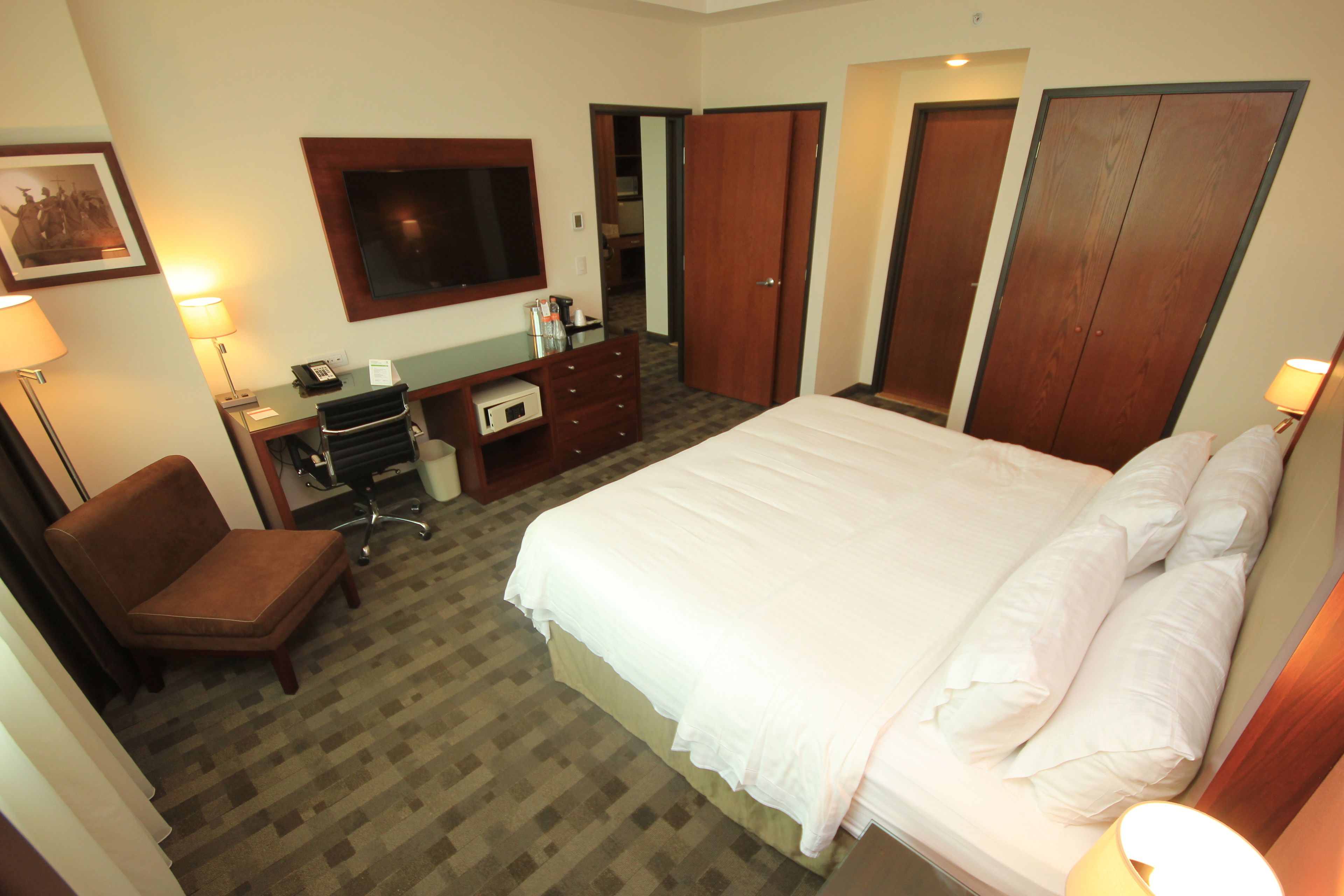 A hotel room with a bed, a desk, a chair, a TV, and a wardrobe.