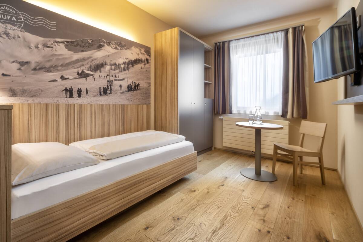 Une chambre d’hôtel moderne, équipée d’un lit, d’une petite table, d’une chaise, d’un téléviseur et d’un grand tableau accroché au mur.