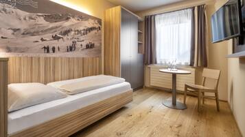 A modern hotel room with a bed, a small table, a chair, a TV, and a large wall-mounted picture.
