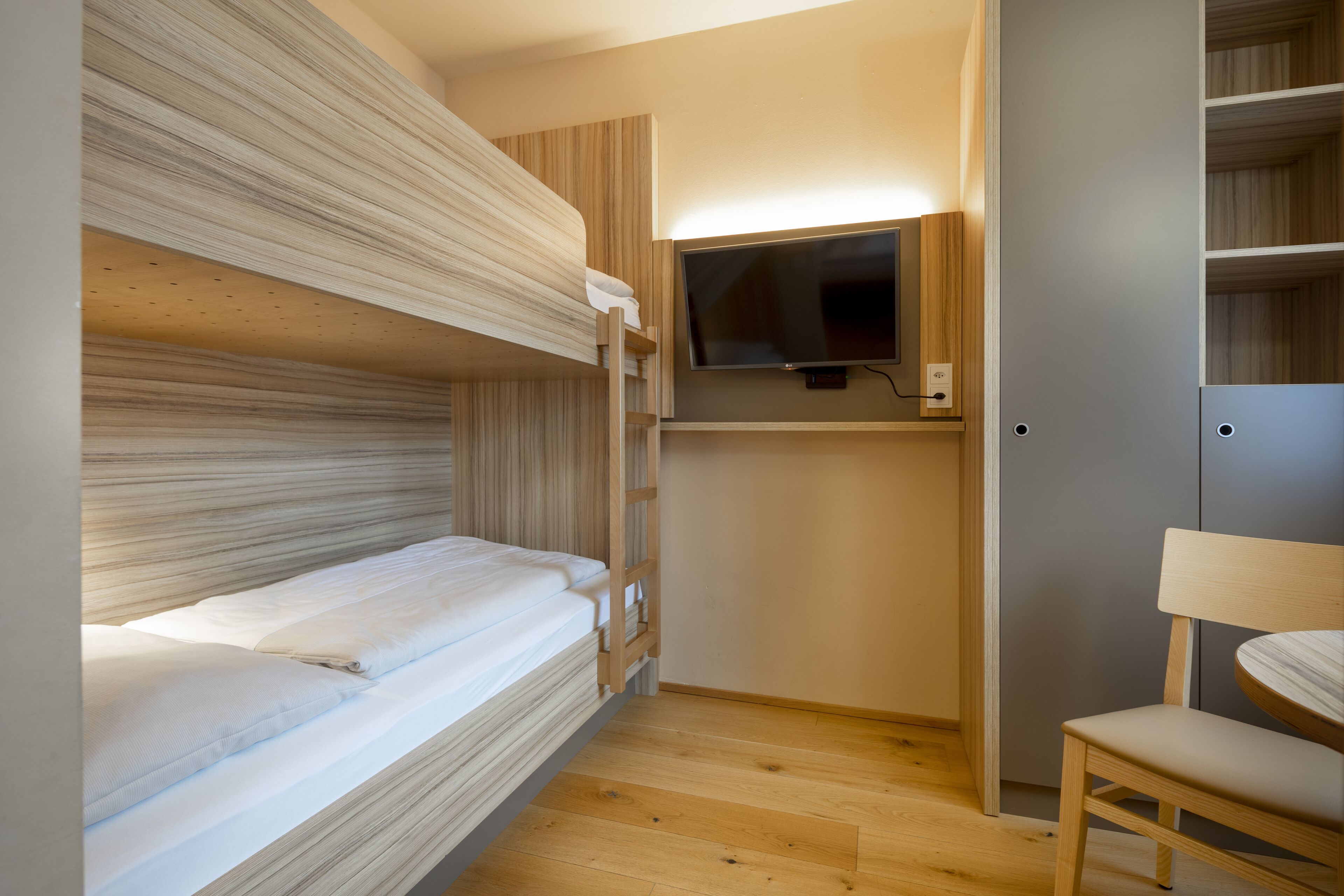 A bunk bed room with a TV and a chair.