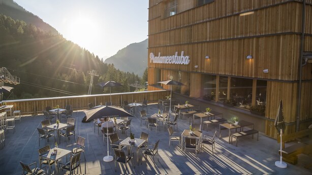 An outdoor patio with tables and chairs, a wooden building with 'Padameestuba' signage, and a mountainous backdrop. - JUFA Hotel Malbun (Triesenberg)