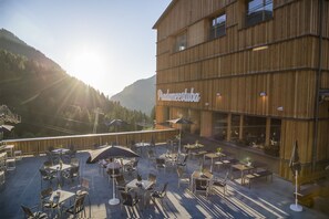 Un patio al aire libre con mesas y sillas, un edificio de madera con el rótulo 'Padameestuba' y un paisaje montañoso de fondo.