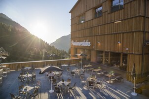 Un patio al aire libre con mesas y sillas, un edificio de madera con el rótulo 'Padameestuba' y un paisaje montañoso de fondo.