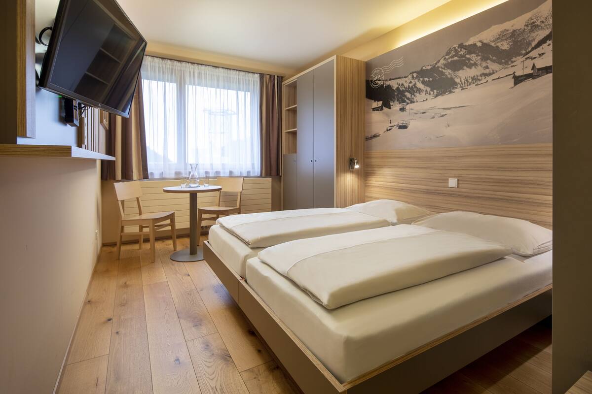Une chambre d’hôtel avec deux lits, un bureau avec une chaise, une télévision et une fenêtre avec des rideaux.