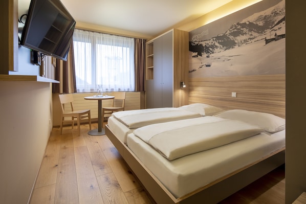 A hotel room with two beds, a desk with a chair, a television, and a window with curtains. - JUFA Hotel Malbun (Triesenberg)