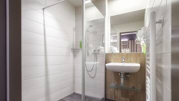 Un baño moderno con cabina de ducha de vidrio, tocador de madera con lavamanos y espejo.