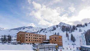 A multi-story building with a wooden facade, located in a snowy mountainous area with ski slopes in the background. - JUFA Hotel Malbun (Triesenberg)