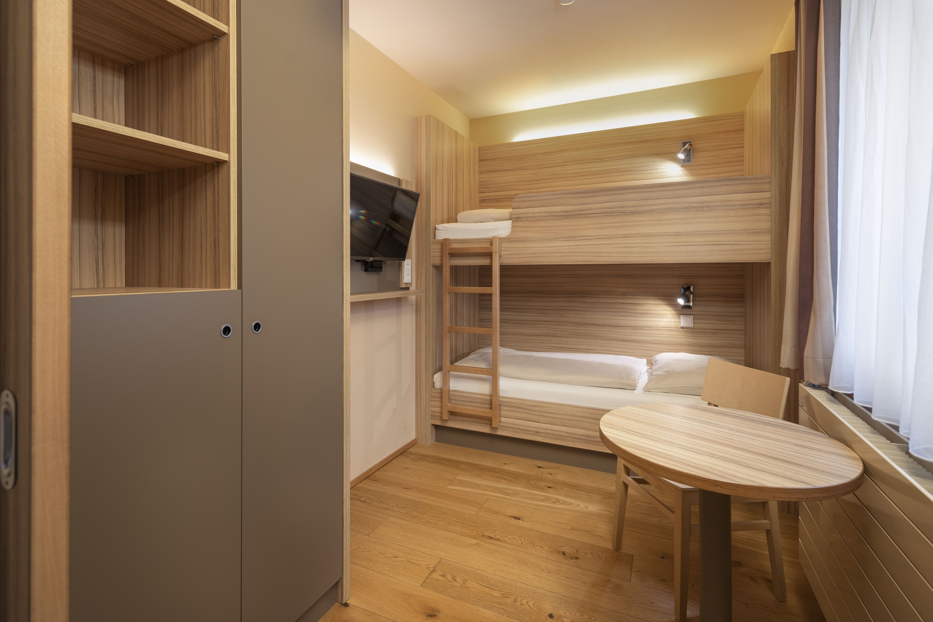 A compact room with a bunk bed, a small table, and a TV.