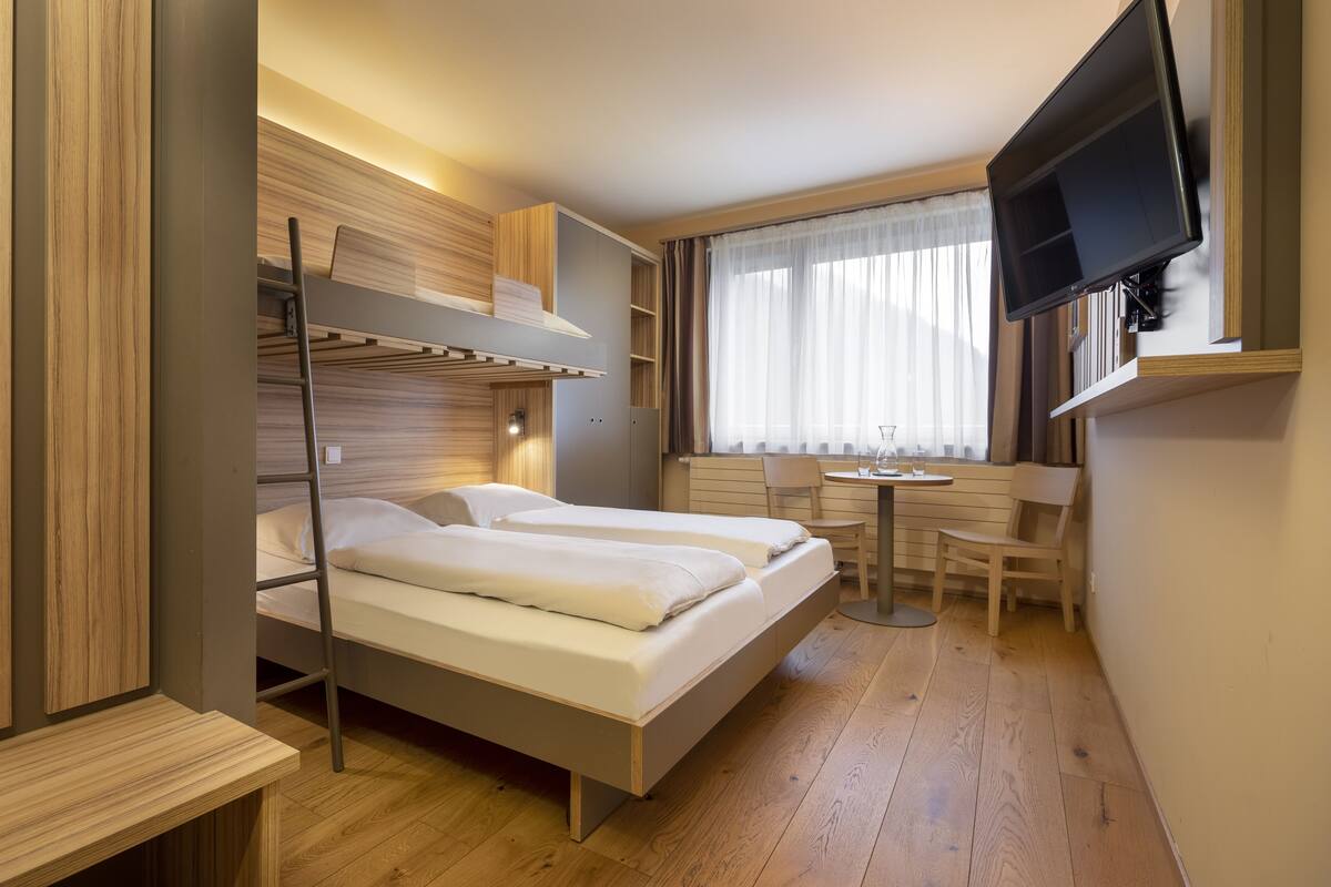 Une chambre d’hôtel compacte équipée de lits superposés, d’un bureau, d’une chaise et d’un téléviseur fixé au mur.
