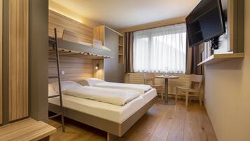 Habitación de hotel compacta con literas, un escritorio, una silla y un televisor montado en la pared.