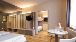 A modern hotel room with a wooden panel wall, a TV, a bunk bed, a round dining table, and a chair. - JUFA Hotel Malbun (Triesenberg)