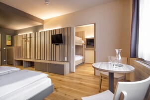 Una habitación de hotel moderna con un panel de madera, televisor, literas, una mesa redonda y una silla.
