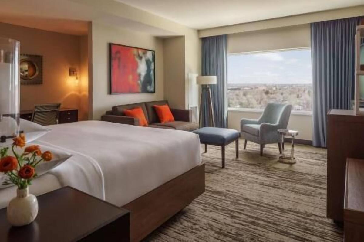 Une chambre d’hôtel dotée d’un grand lit, d’un coin salon avec un fauteuil et un canapé, d’un bureau et offrant une vue sur la ville.