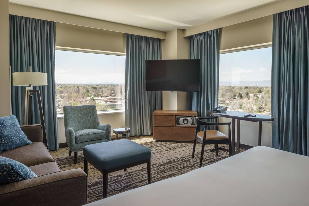 Une chambre d’hôtel avec un grand lit, un canapé, un bureau avec une chaise, une télévision et une vue sur un paysage par les fenêtres.