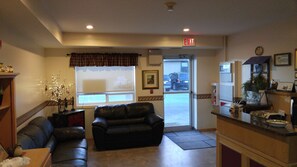 A lobby with a leather sofa, a reception desk, a window with a view of the outside, and an exit sign.