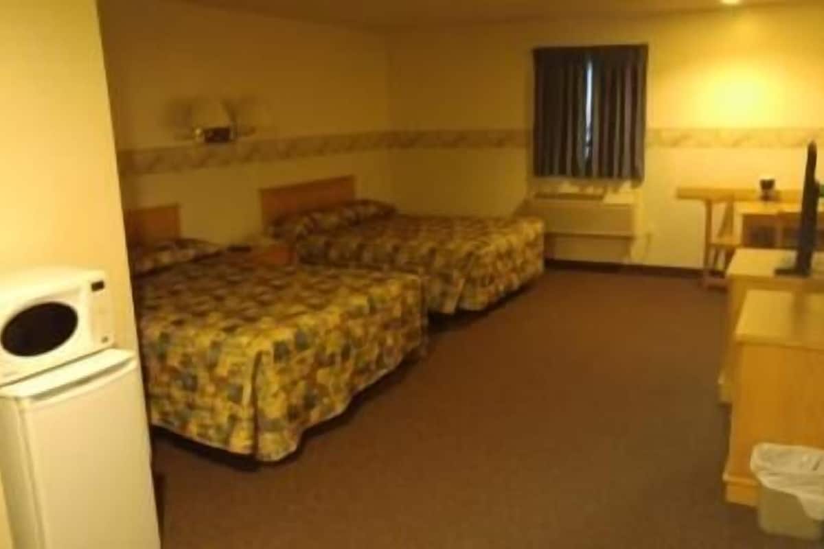 A hotel room with two beds, a small desk, a chair, a television, and a washing machine.