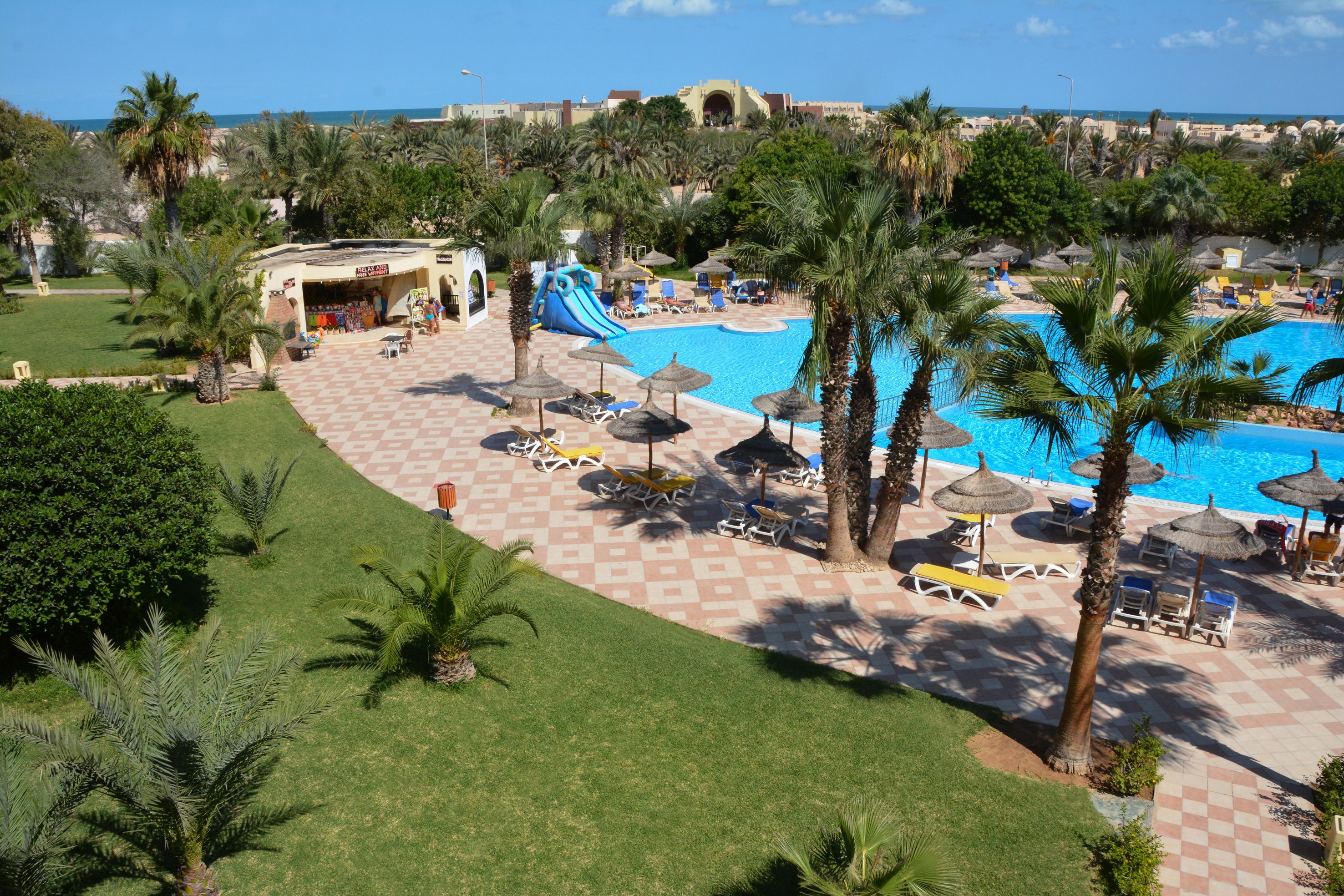 A resort with a swimming pool, palm trees, and a children's play area.