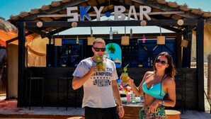 Un bar appelé « 5KY BAR », doté d’une structure en bois rustique, de tabourets et d’un comptoir où sont servis des boissons.