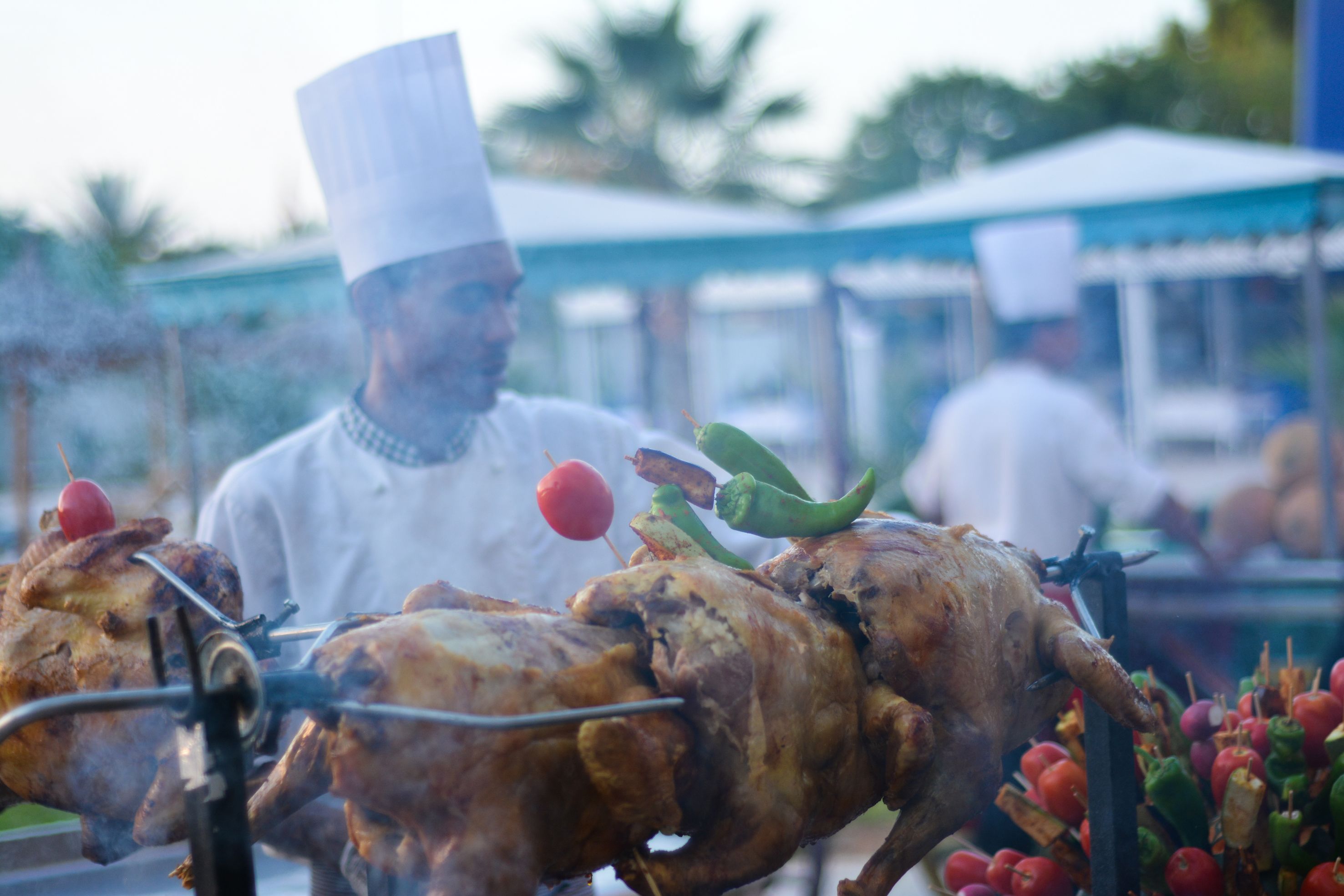 A chef grilling meat with skewers, surrounded by a market setting.