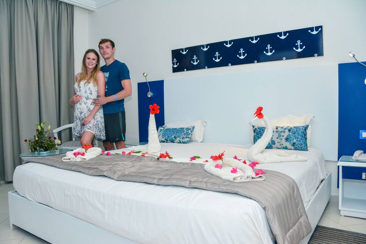 A hotel bedroom with a bed, pillows, a nightstand, and a wall with anchor decorations.