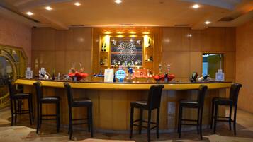 Una zona de bar con una barra alargada, varios taburetes y una gran variedad de botellas y vasos.