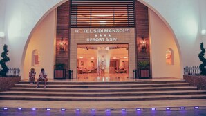 L’entrée de l’hôtel Sidi Mansour Resort & Spa, avec sa façade moderne en forme d’arc et son intérieur bien éclairé.