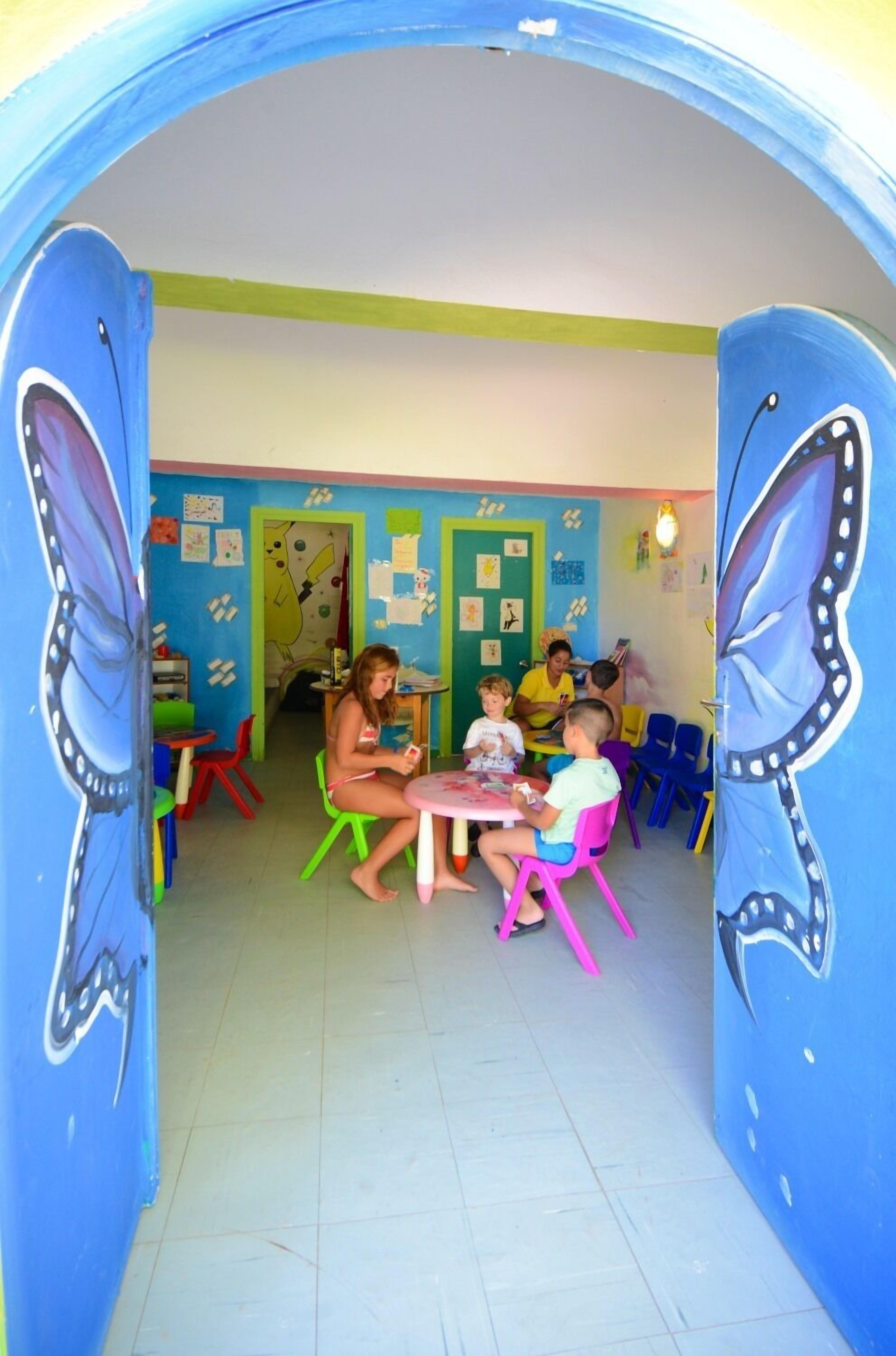 A classroom with children seated at tables, colorful chairs, and educational posters on the walls.