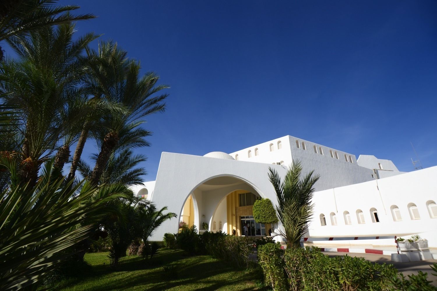 A modern building with a large central archway, surrounded by palm trees and a well-maintained lawn.