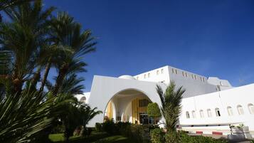 A modern building with a large central archway, surrounded by palm trees and a well-maintained lawn.