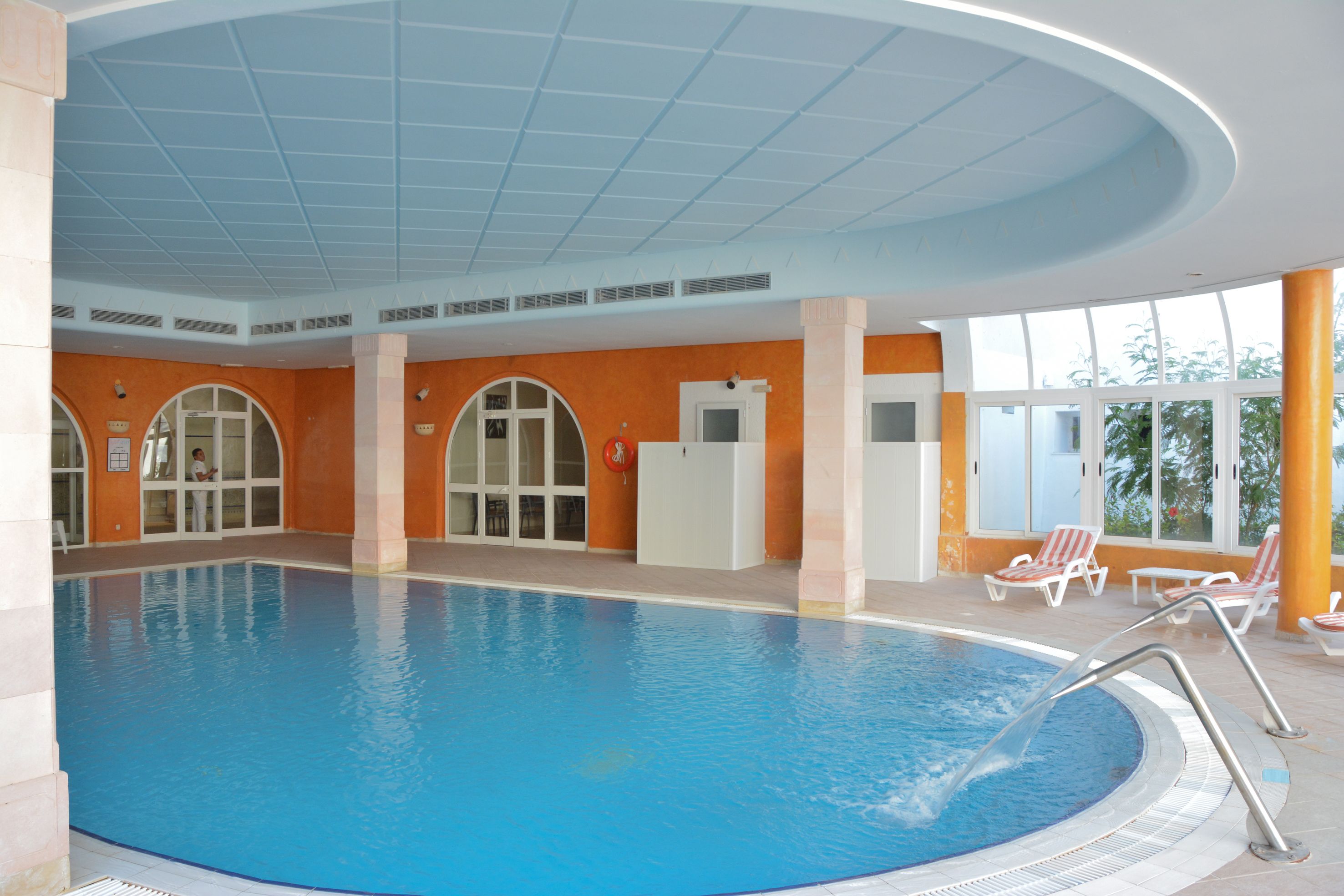 Una piscina interior con agua cristalina, rodeada de paredes naranjas y columnas blancas.